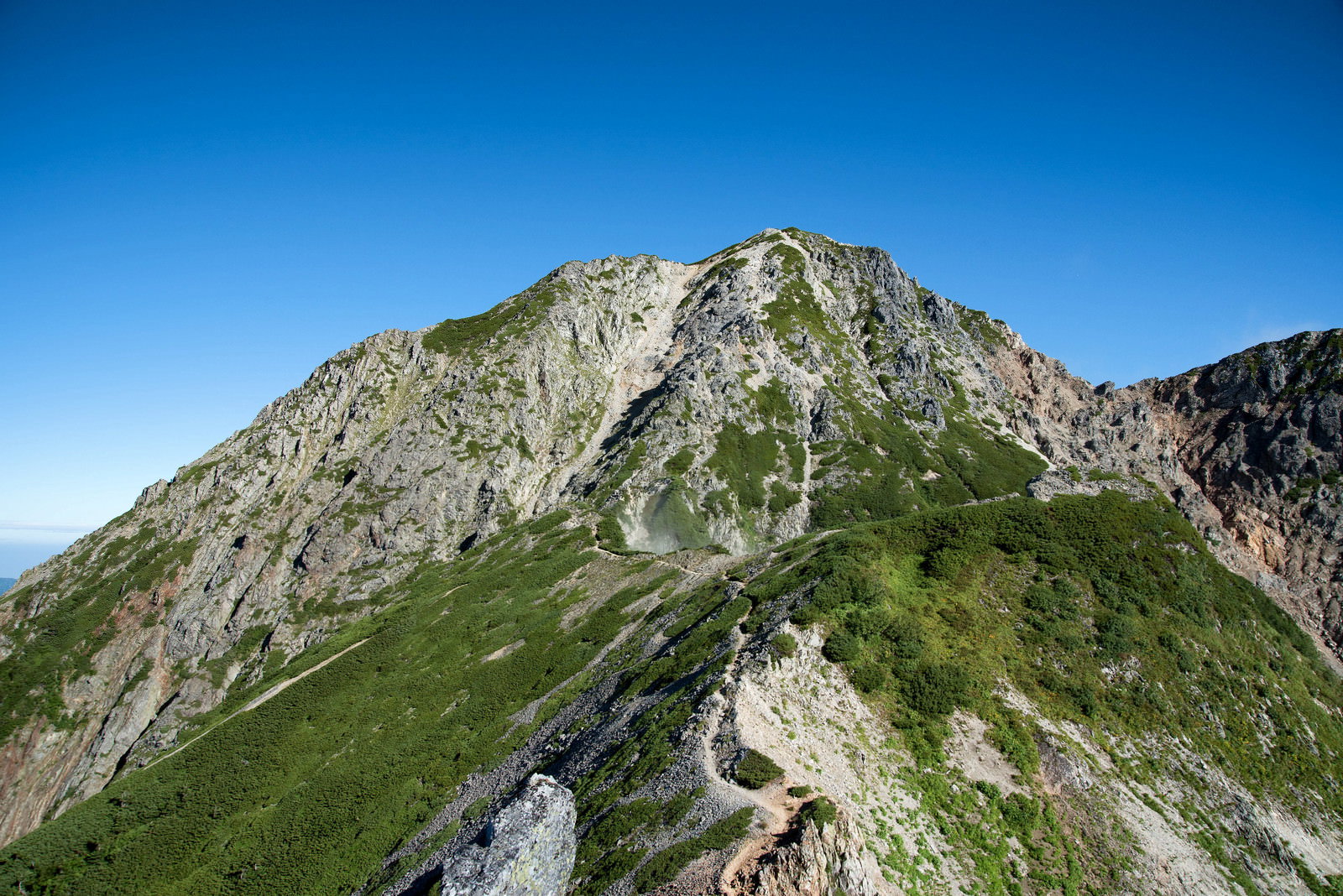 青空の下に聳え立つ険しい岩尾根と、稜線上を通る登山道