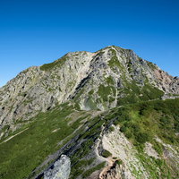 青空の下、聳え立つ岩尾根と八峰キレットの登山道の写真