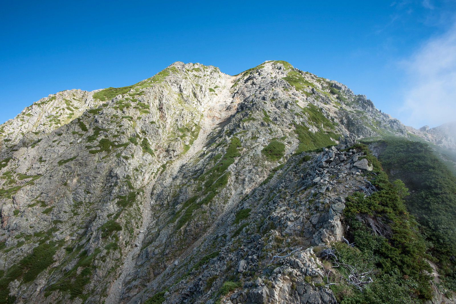 切り立った岩稜が連なる山の尾根に登山道が続く風景