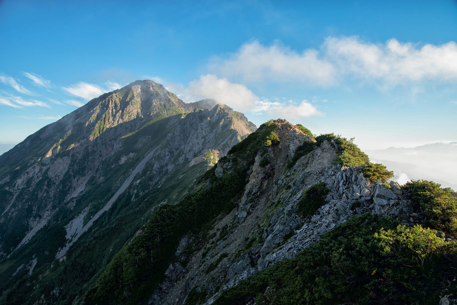 険しい岩場が連続する岩尾根が遠くまで続く登山道の風景