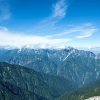 緑溢れる山々にかかる雲と八峰キレットの連峰の写真