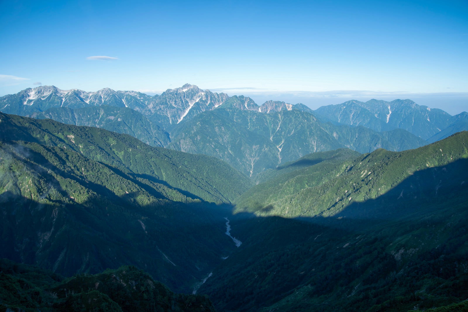 青空の下、連なる山脈の尾根筋に陽光が差し込む光景