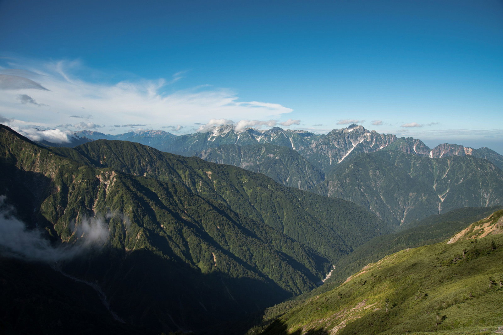 青空の下に緑の山々と険しい岩尾根が連なる山岳風景