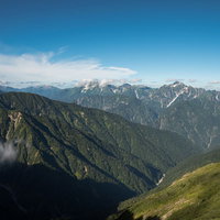 晴れ渡る空と遠くに見える岩尾根、八峰キレットの連峰の写真