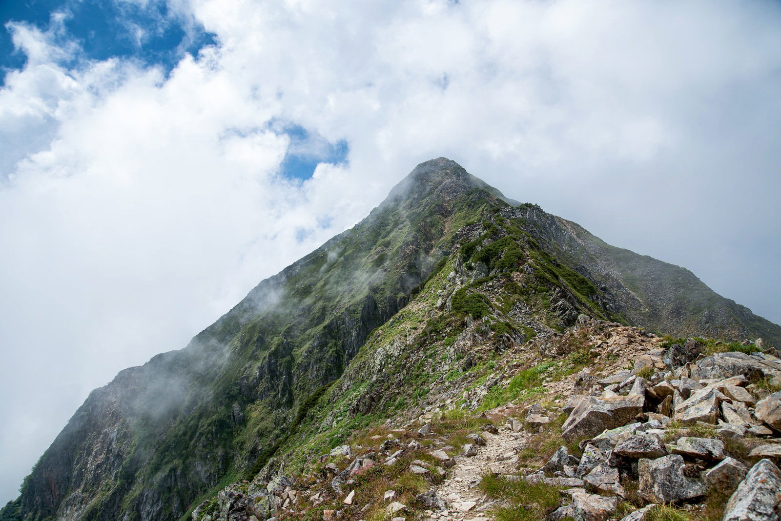 雲に包まれた山頂へ向かう岩場の登山道と石積み