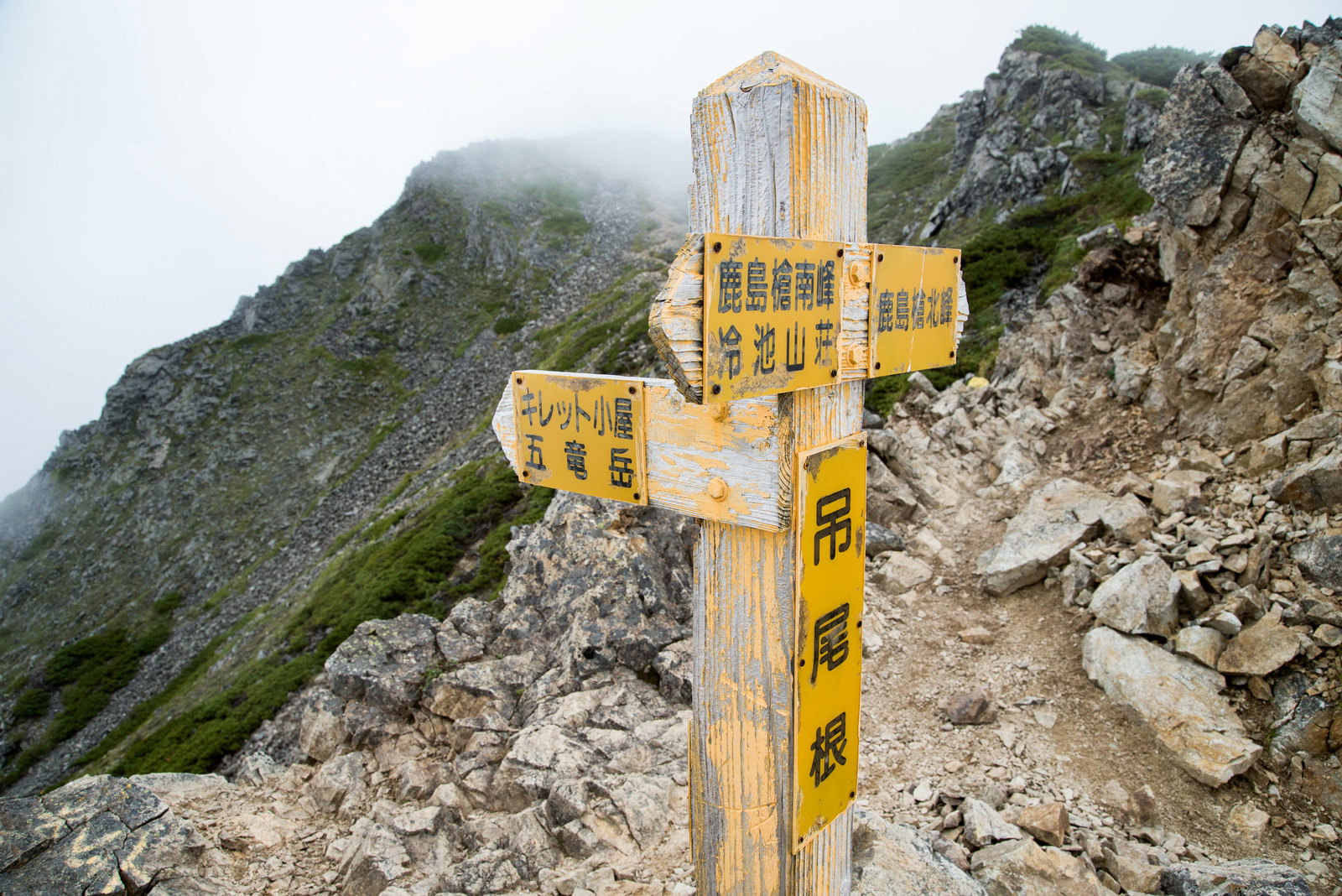 険しい岩場の登山道に設置された黄色いキレット小屋の指導標