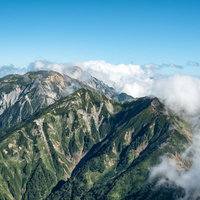 八峰キレット縦走路で見る山々を覆う雲と青空の写真
