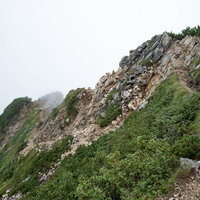 雲の壁に突き進む八峰キレットの登山道を進む登山者の写真