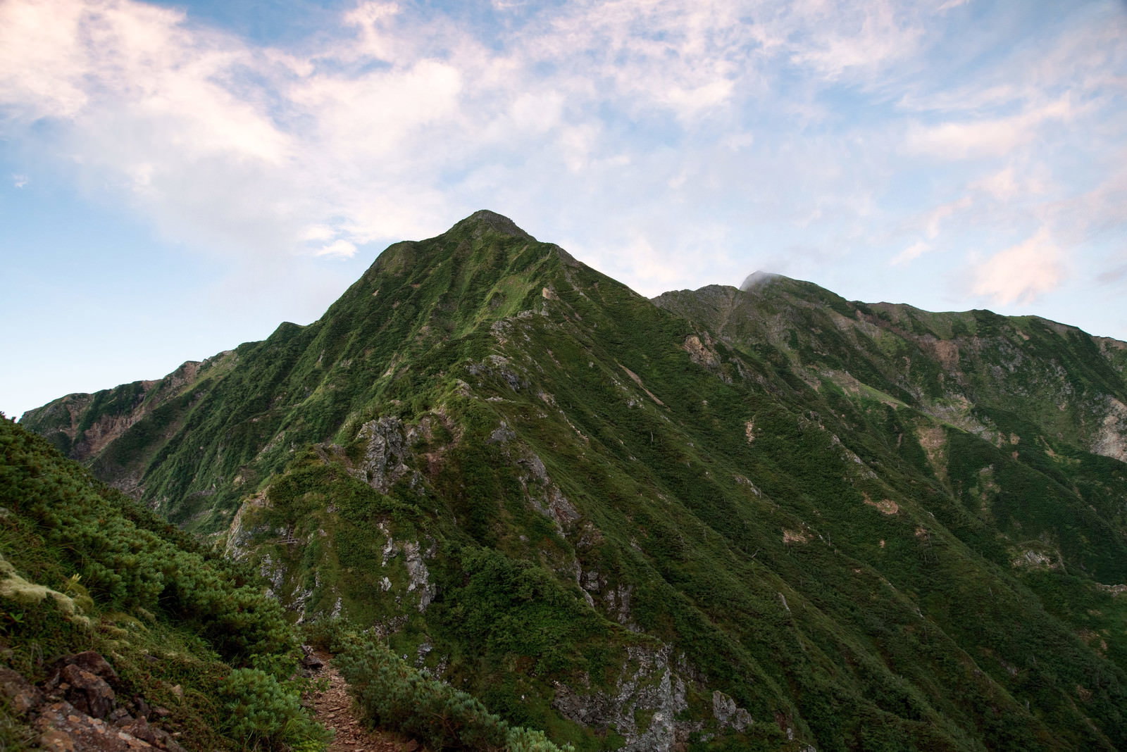 夕焼け空の下に緑豊かな険しい山稜が連なる風景