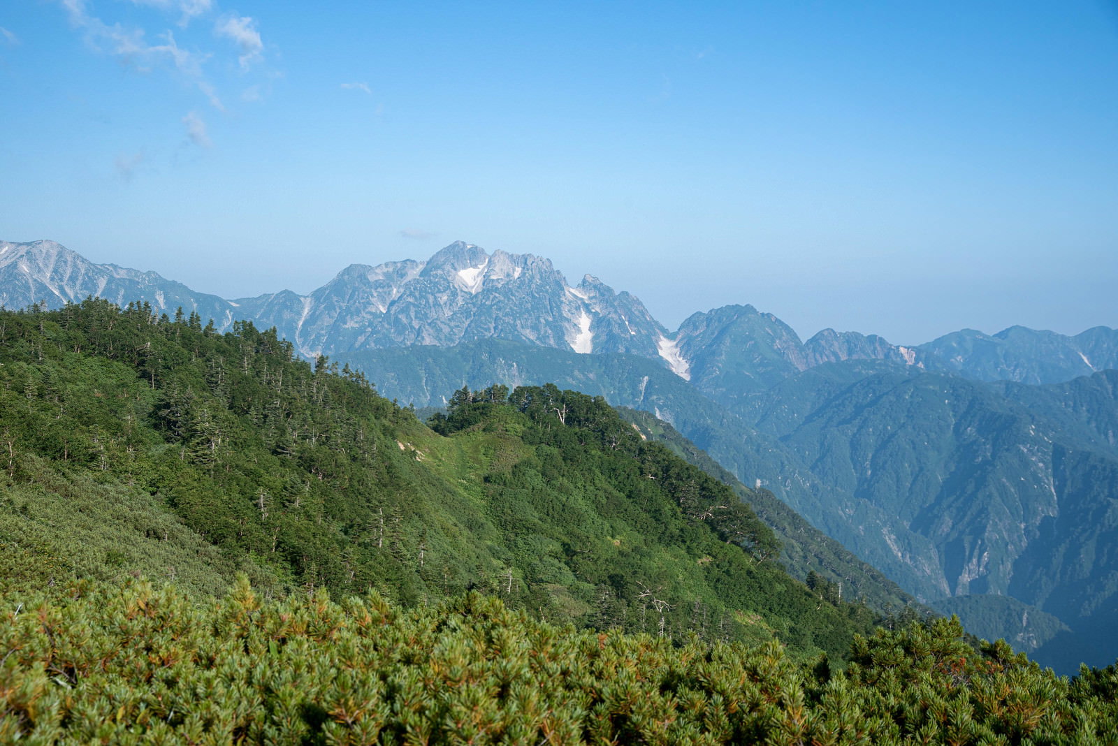 緑の稜線越しに霞んで見える連峰の山々と青空