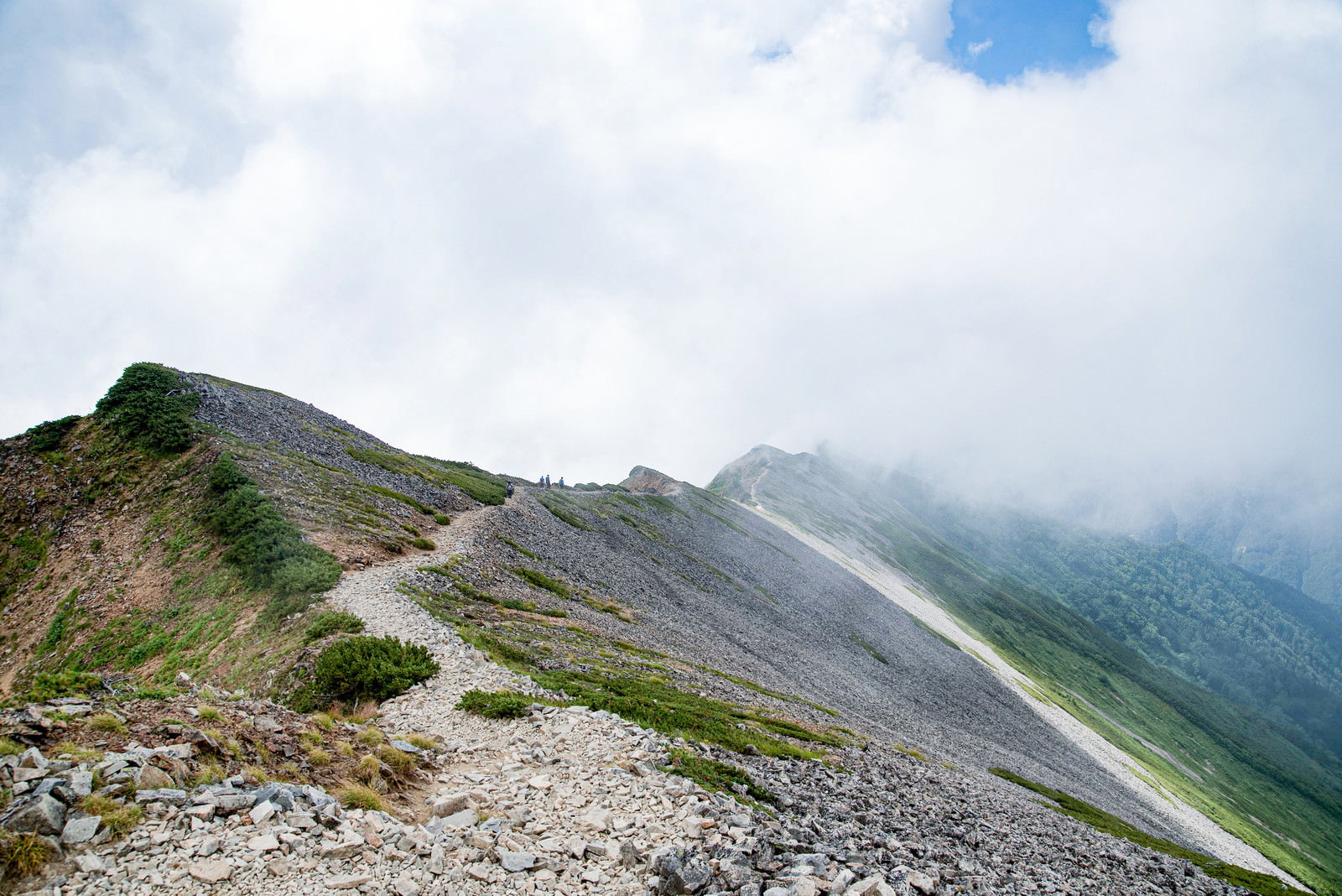 雲に包まれた稜線のガレ場を歩く登山者の後ろ姿