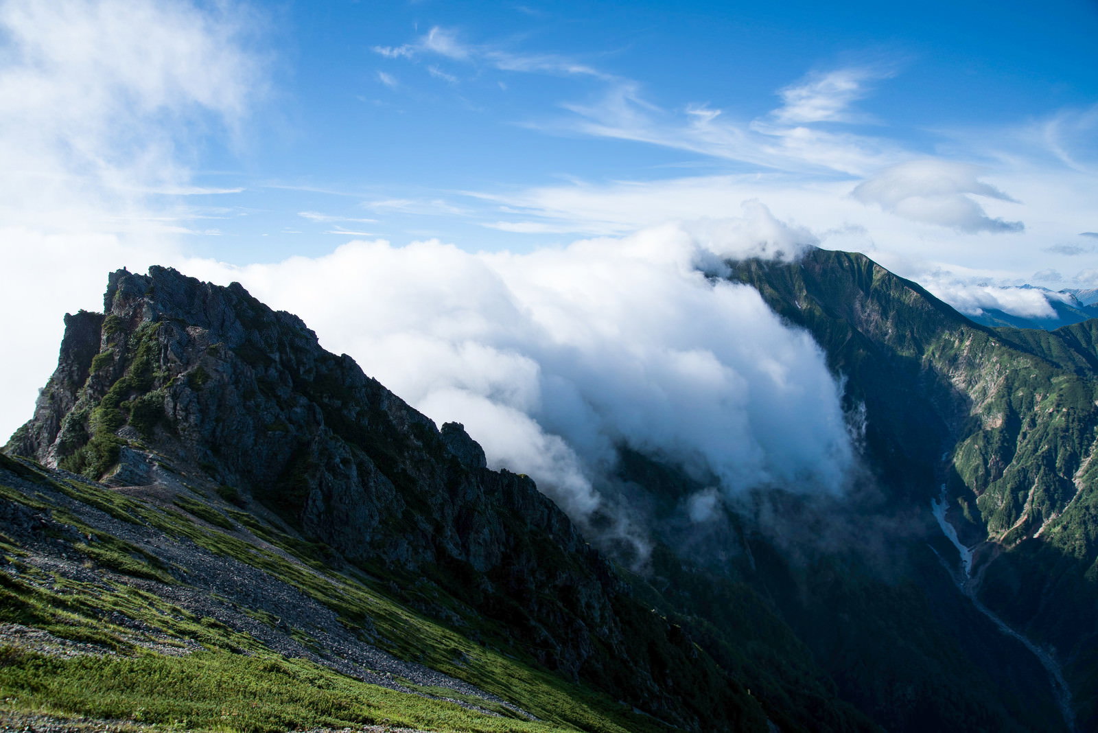 険しい岩稜の尾根に白い雲が流れ込む山岳風景