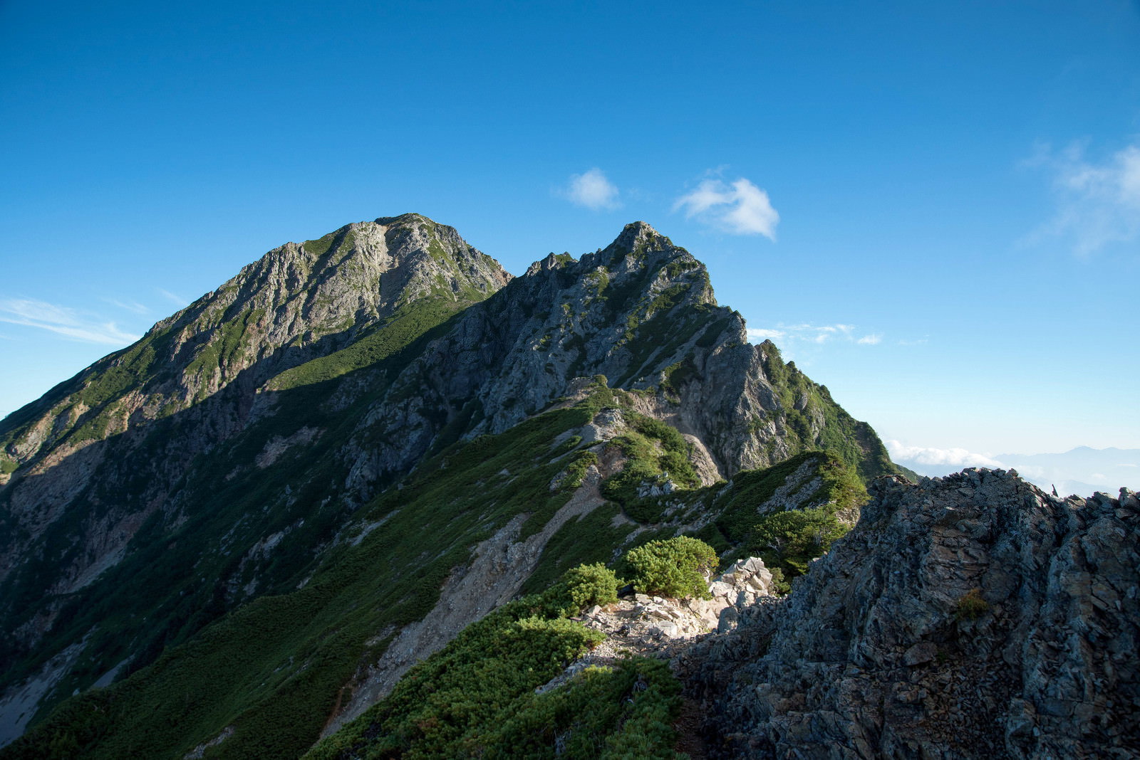 険しい岩稜帯の登山道で岩尾根から長い影が伸びる山岳風景