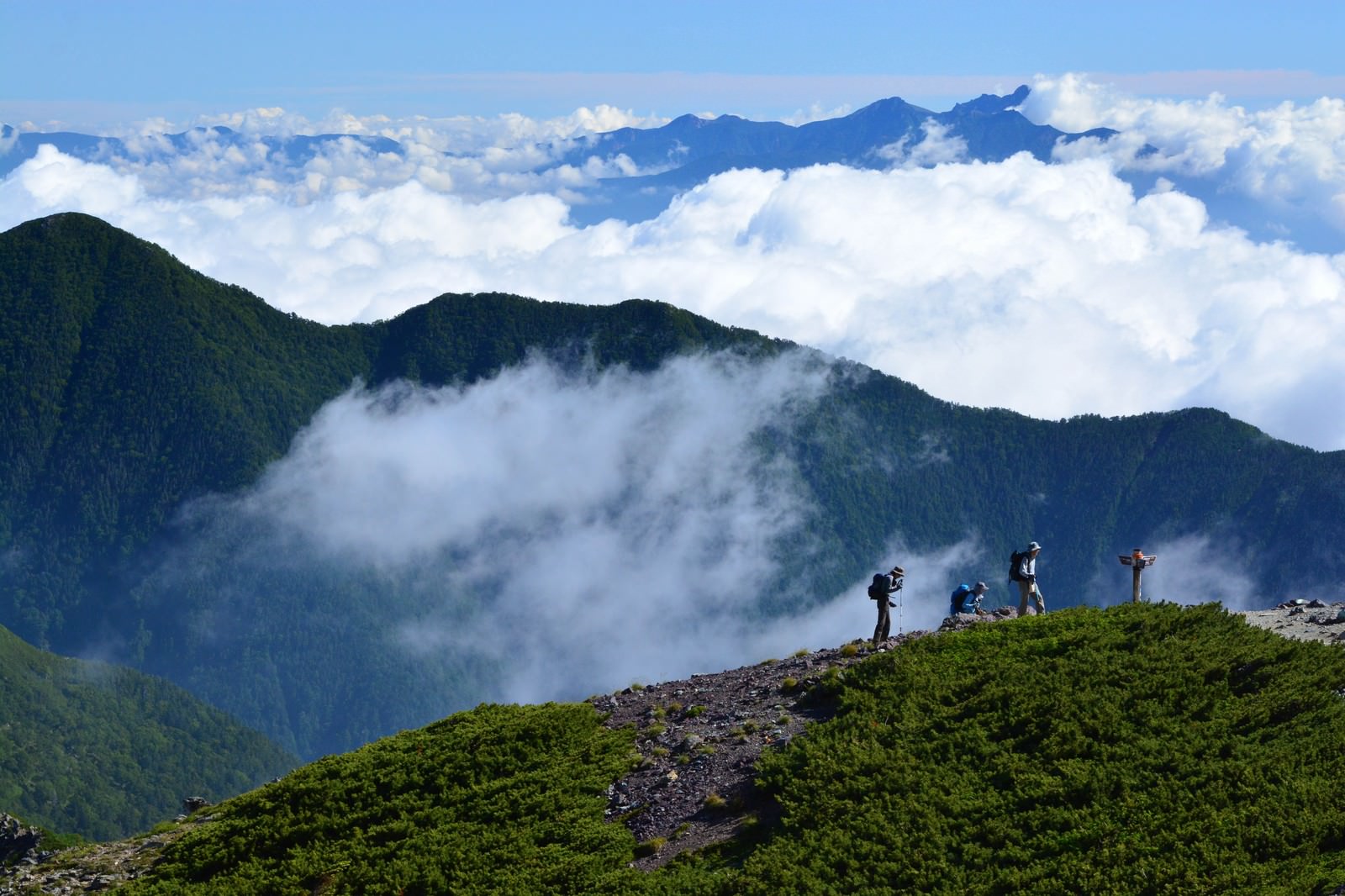 雲海が広がる山間の登山道を歩く登山者たちの風景