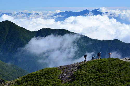 雲海を見下ろす山間の登山道を歩く登山者たち