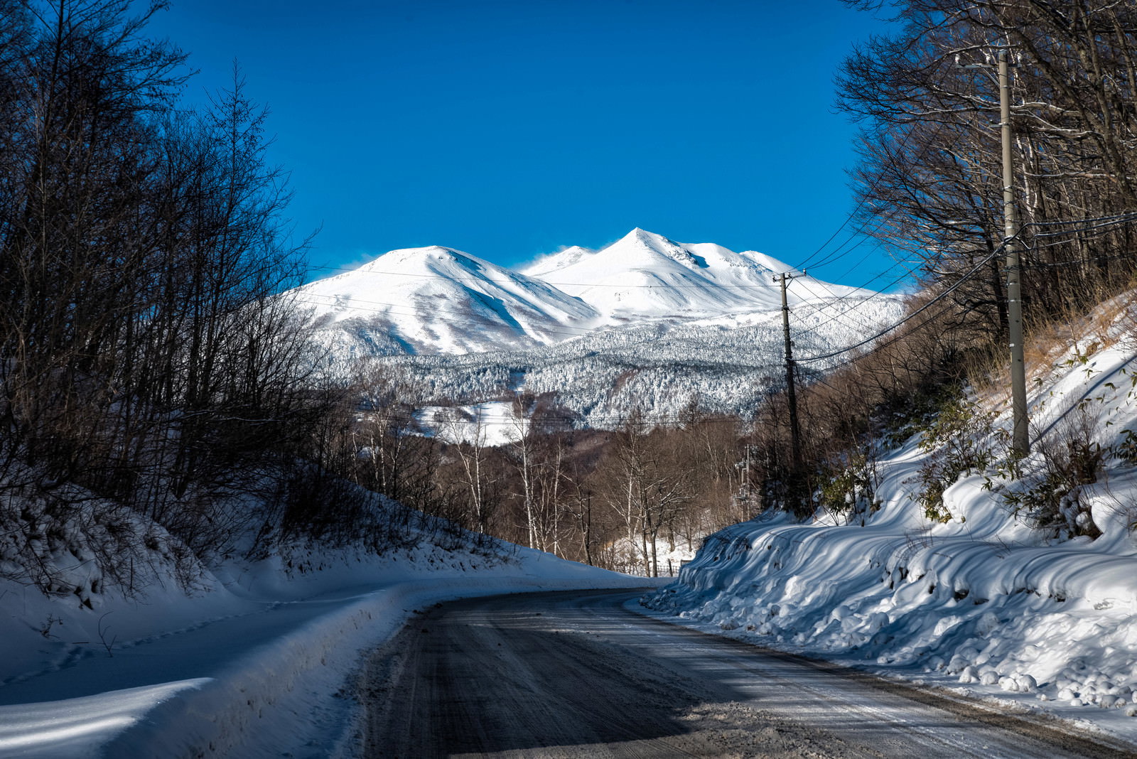 青空の下、残雪に覆われた道路が乗鞍岳の雪山へと続く冬景色