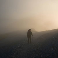濃霧に包まれた山道を歩む登山者のシルエットの写真