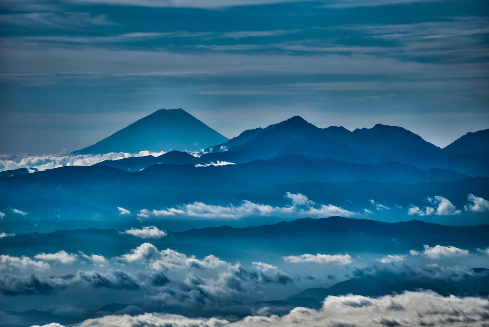 雲海の上に浮かぶ山峰のシルエットが青空の下に連なる風景