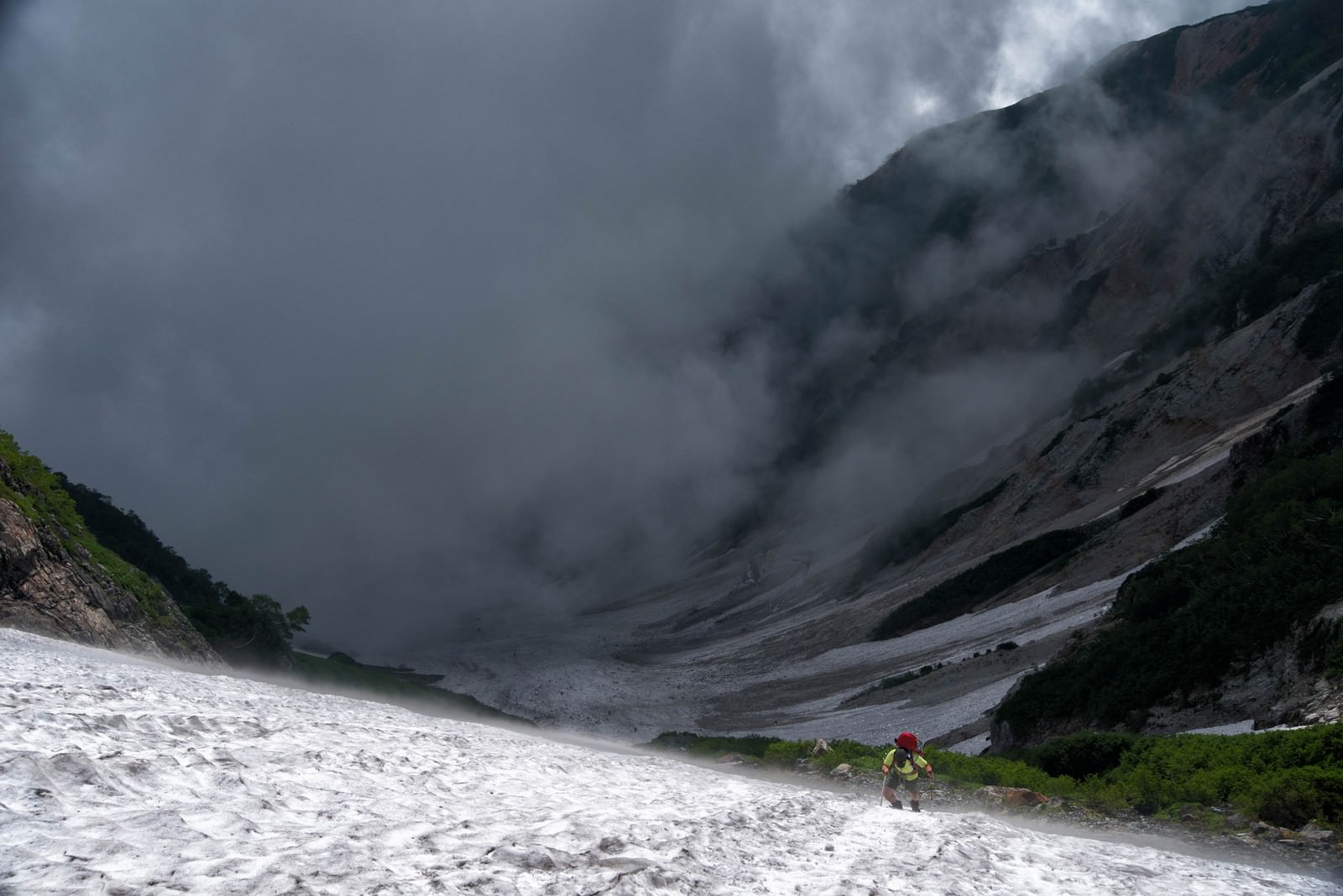 霧に包まれた山の雪渓を登る登山者の姿