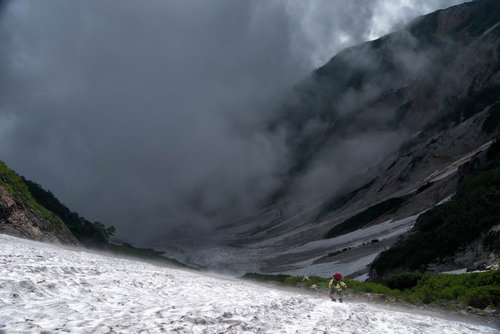 霧に包まれた大雪渓をよじ登る登山者たちの冬山登山