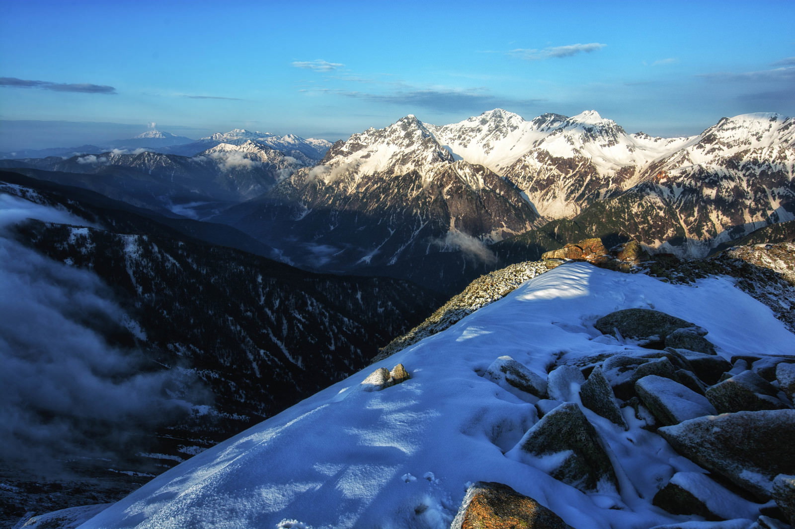 雪に覆われた常念岳山頂から見える雪山と青空の風景