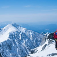 雪に覆われた山々の中で赤いウェアの登山者が立つ雪山の写真