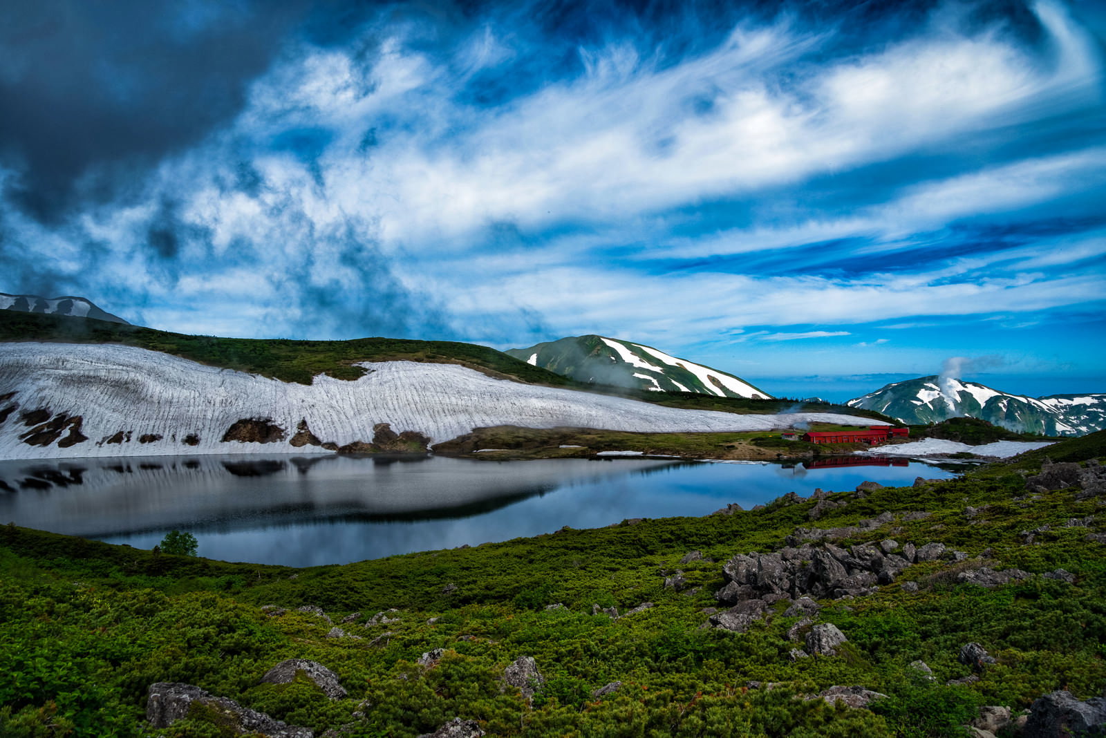 白馬大池の湖面に映る山荘と北アルプスの山々、残雪のある風景