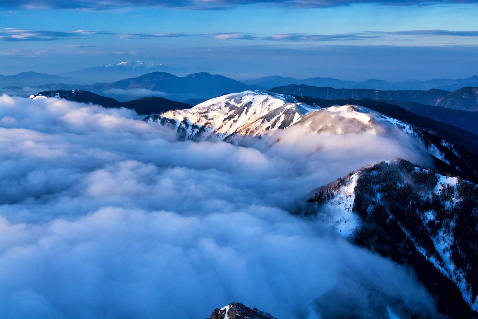 雲海に包まれた雪化粧の蝶ヶ岳と青空が広がる冬の北アルプスの風景
