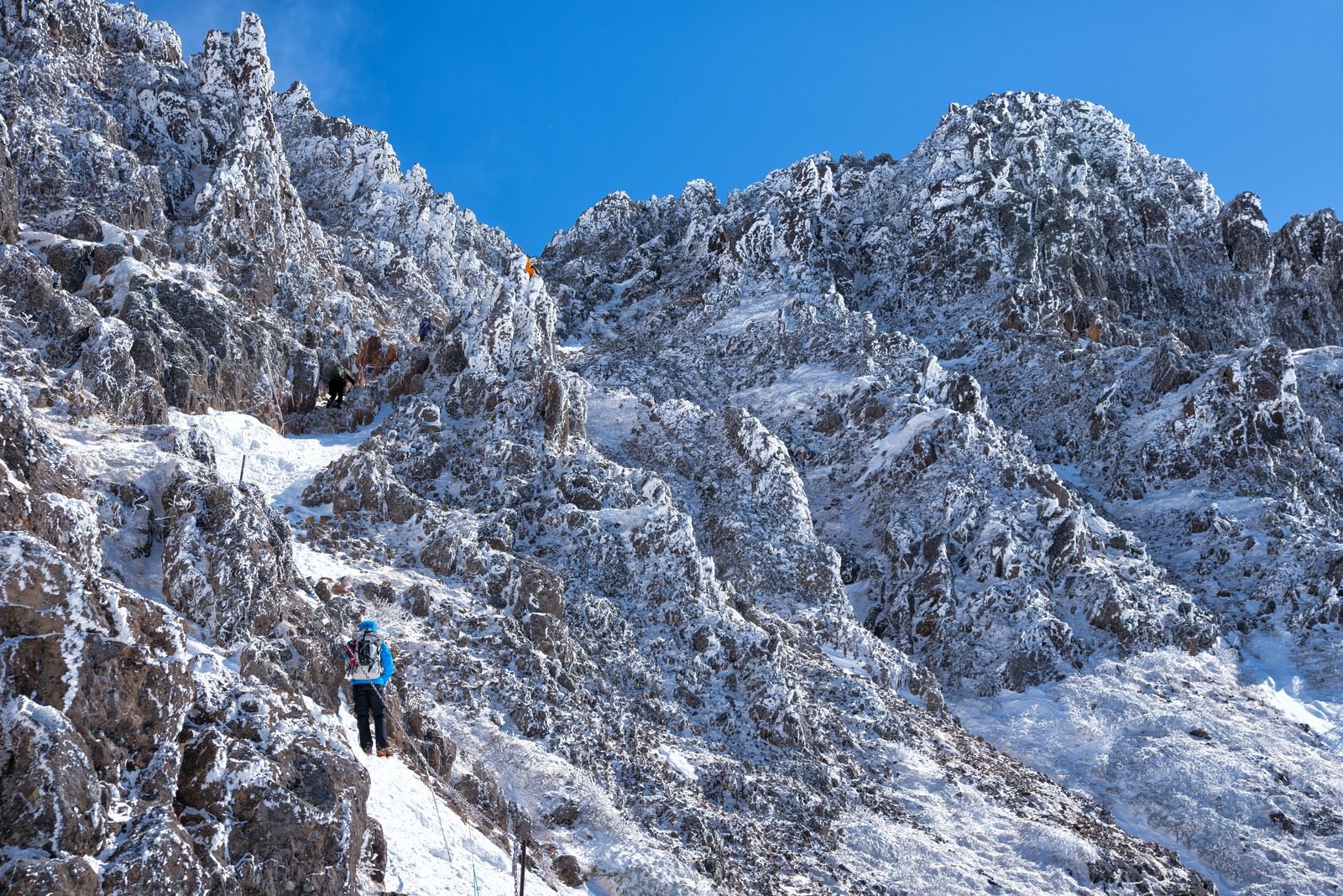 雪に覆われた険しい岩壁を登る登山者と青空