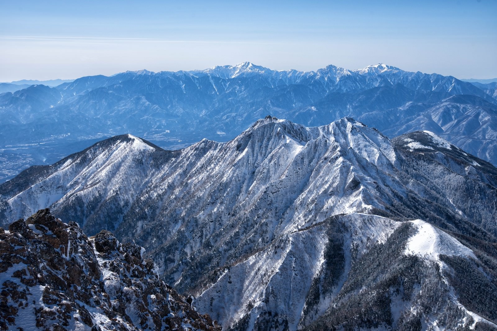 雪に覆われた権現岳と南アルプスの山々が青空の下に連なる冬の山岳風景