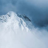 灰色の雲の切れ間から姿を出した阿弥陀岳（八ヶ岳南部の雪山）の写真