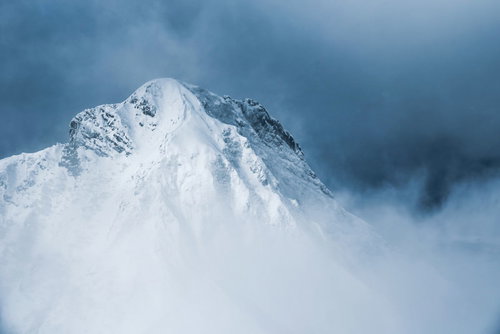 灰色の雲の切れ間から姿を出した阿弥陀岳（八ヶ岳南部の雪山）