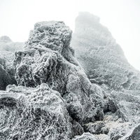 厳冬の岩肌に張り付く氷と霧のモノクロ風景の写真