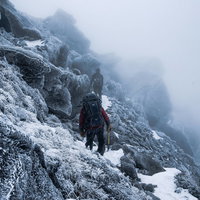 視界不良の霧に包まれた雪山と登山者の冬季登山風景の写真