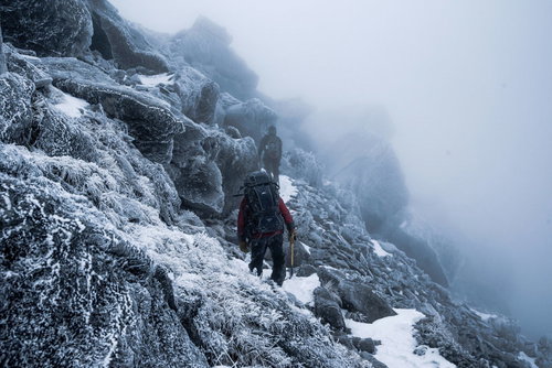 視界不良の霧に包まれた雪山と登山者の冬季登山風景