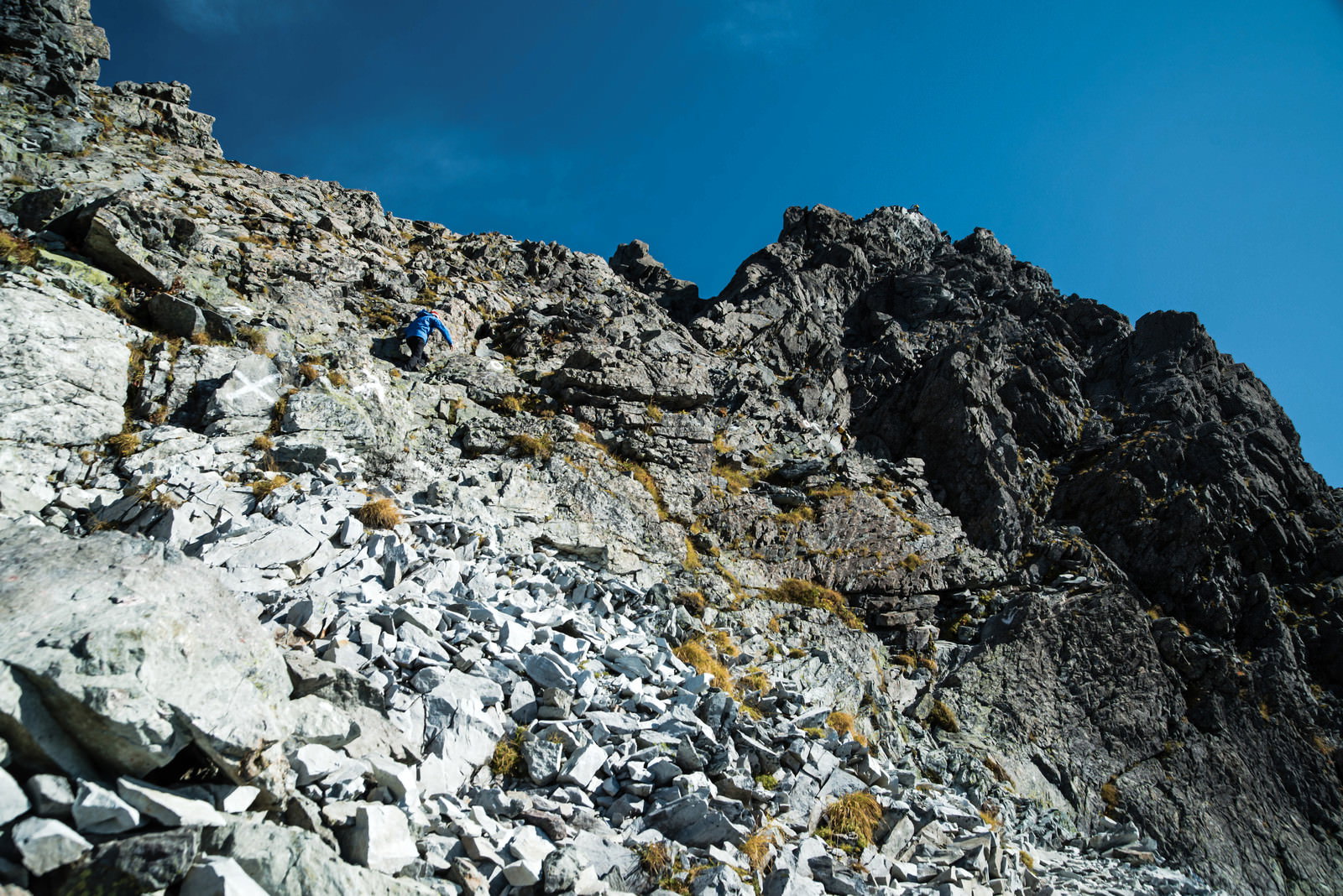 青空の下、槍ヶ岳の険しい岩壁を登る登山者の姿