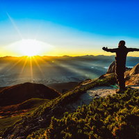 朝日を全身に浴びて両手を広げる山頂の登山者の写真
