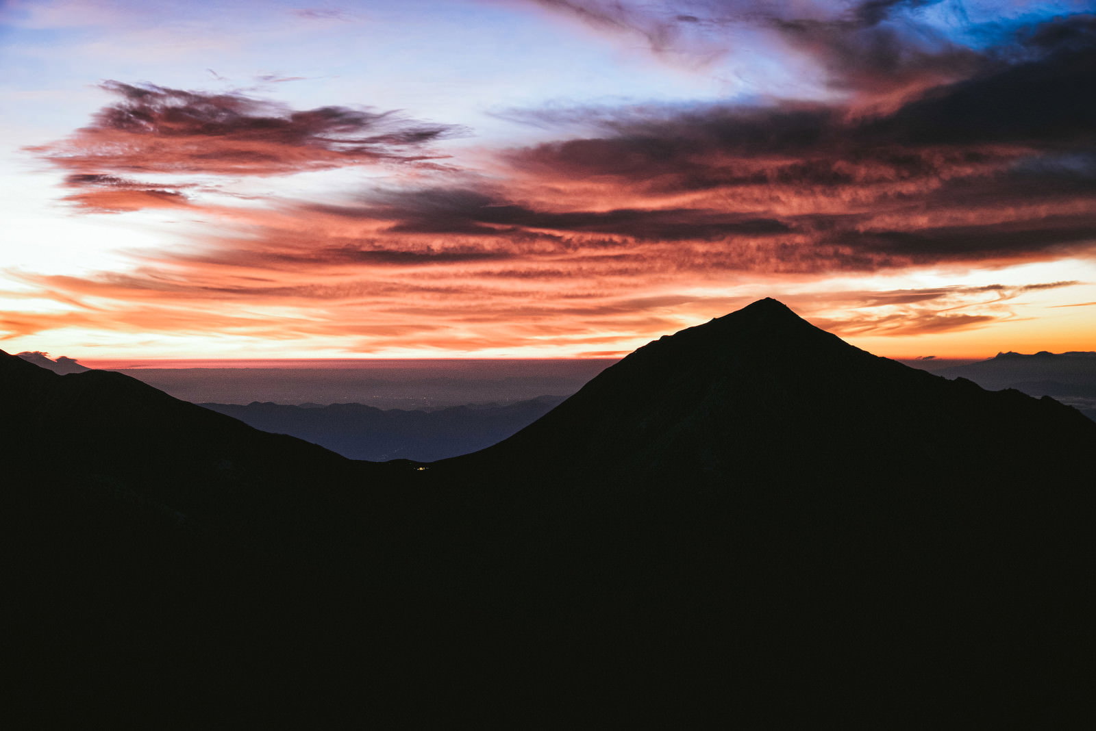 The silhouette of Mount Jonen in the Hida Mountains stands against the sky, which is painted in orange and pink by the morning glow.