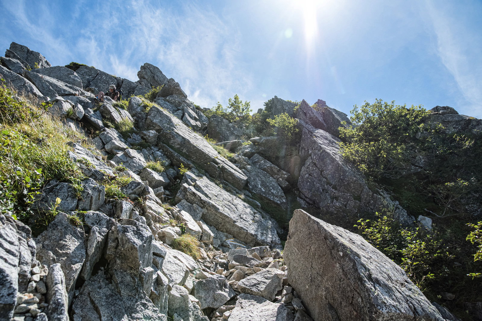 不帰キレットの急峻な岩場を登る登山者と青空