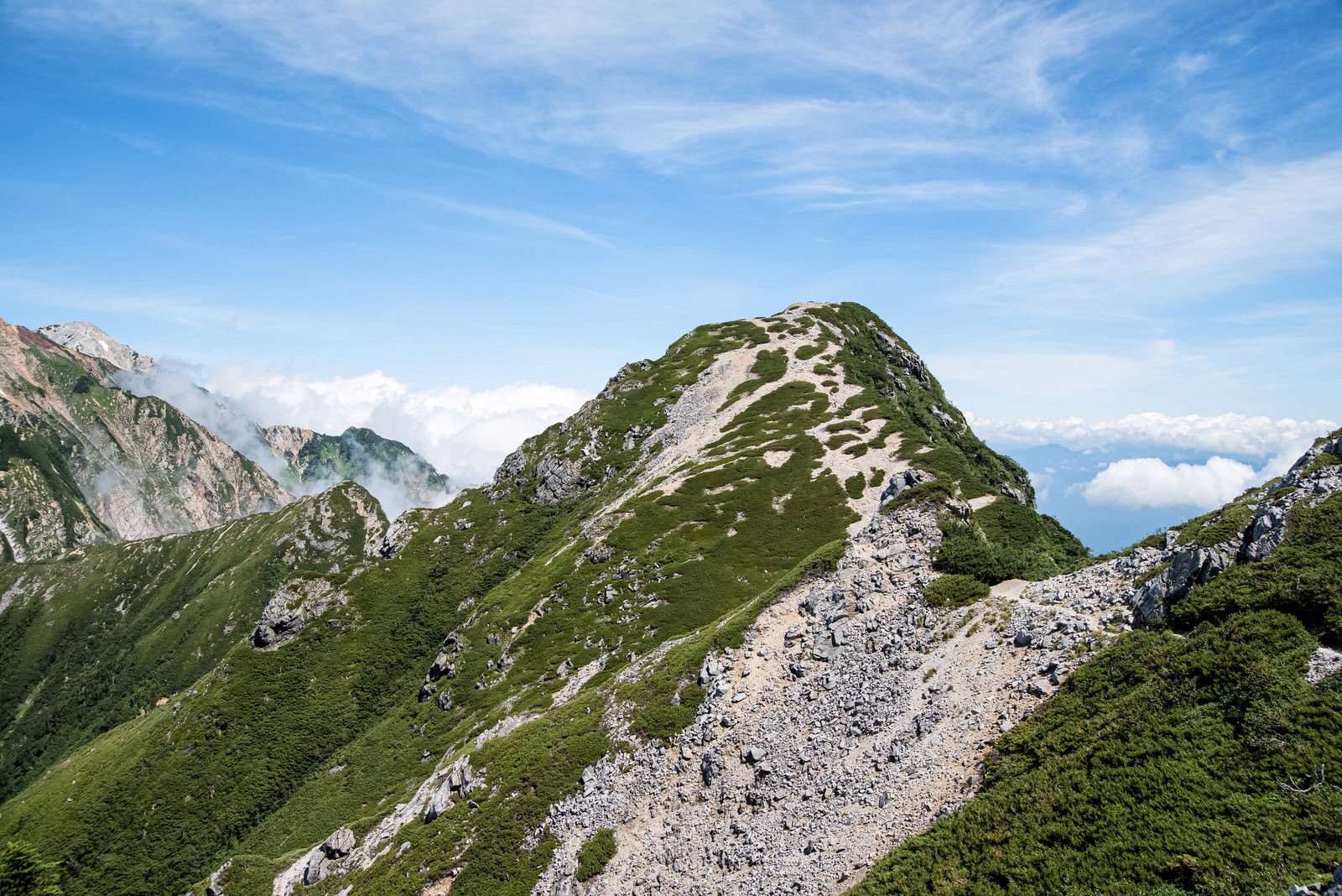 緑の山肌を登る登山道と青空が広がる山岳風景