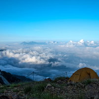 山の斜面に設営したテントと眼下に広がる雲海の写真