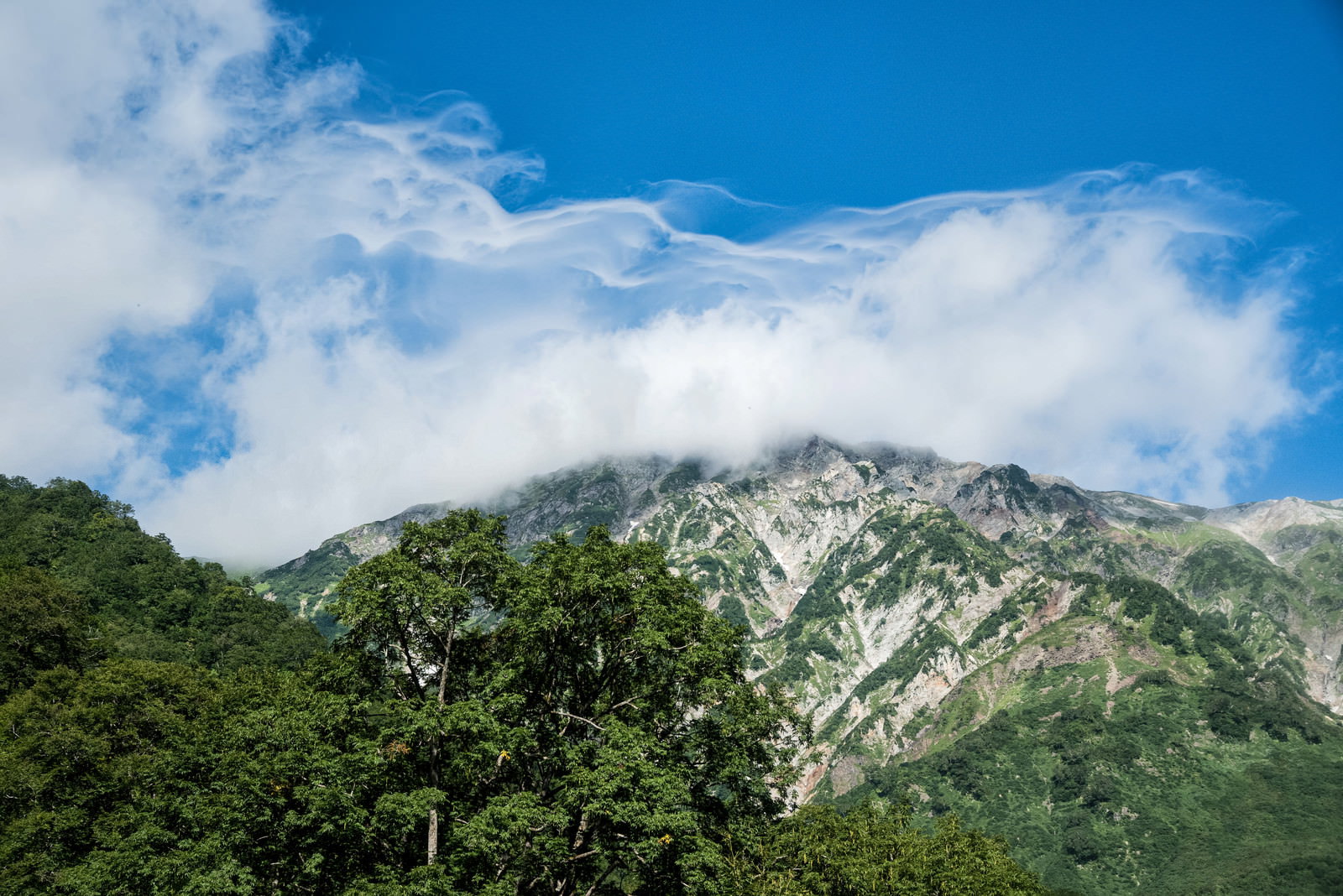 雲に包まれた白馬岳の山岳風景、青空と白い雲が流れる