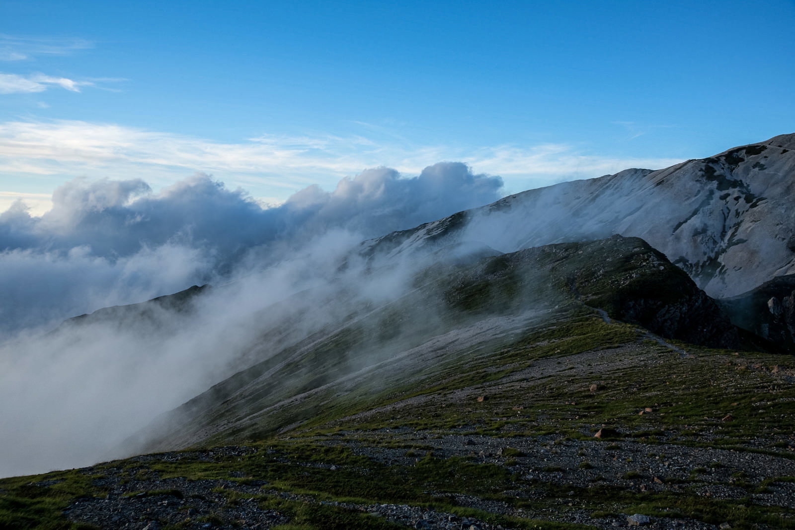 雲海に包まれた山稜線と青空が広がる登山道の風景