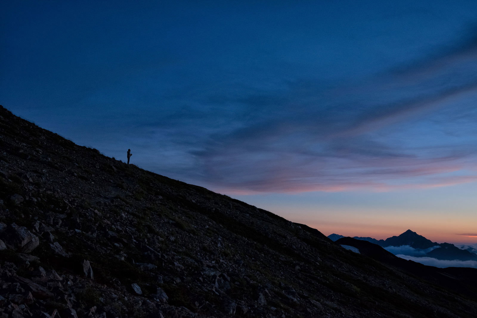 夕焼け空をバックに岩稜帯を歩く登山者のシルエット