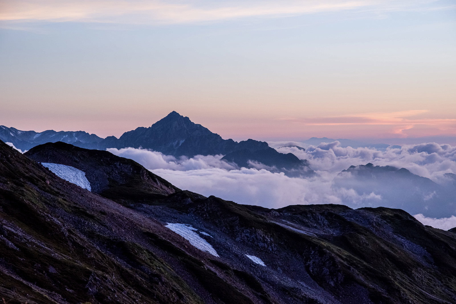 雲海の上に聳える剱岳が夕焼けでピンク色に染まる山岳風景
