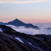 キレット縦走で見る夕焼け色に染まる剱岳と北アルプスの山並みの写真
