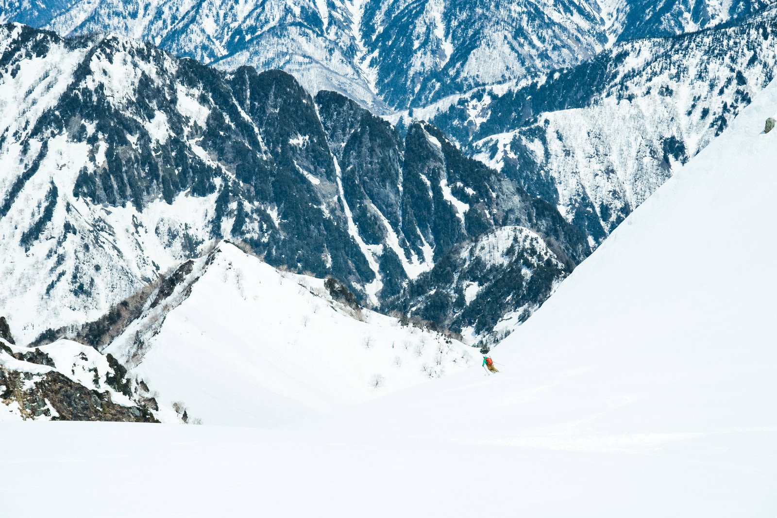 雪山の斜面を滑るスキーヤーとシュプールが描かれた雪景色