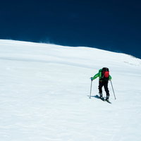 青空に向かって歩みを進めるスキーヤーの後ろ姿の写真