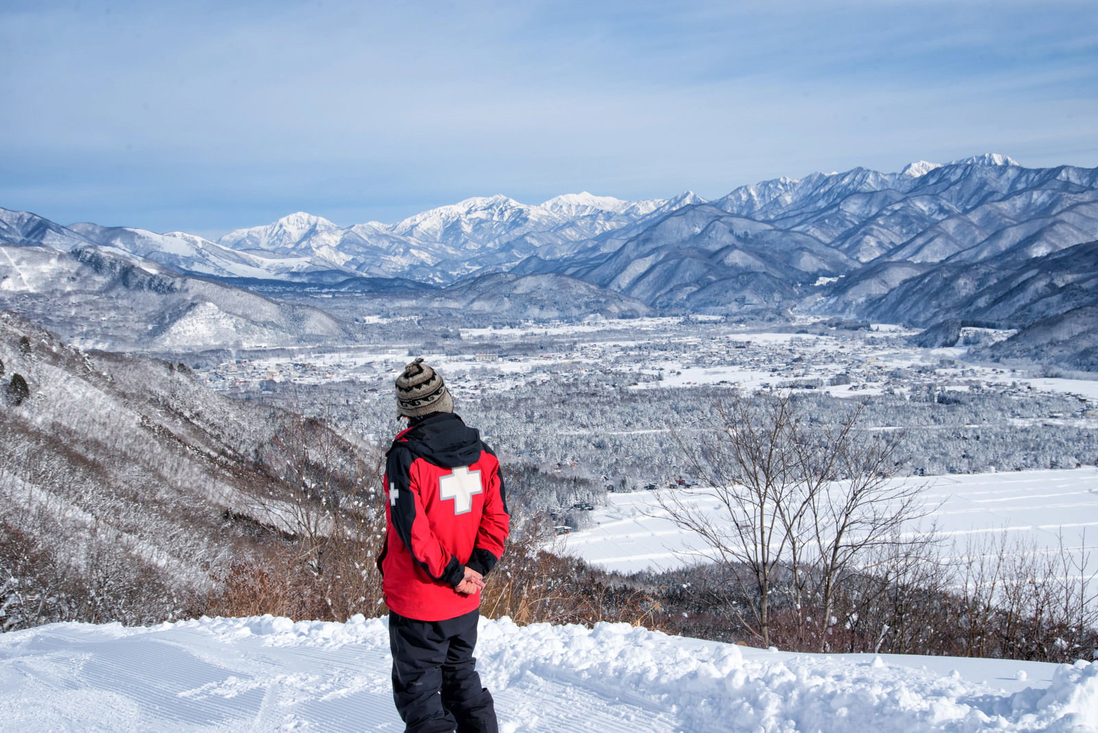 雪山を背景に赤いウェアを着たスキー場パトロール隊員が立っている