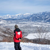 スキー場のパトロール隊員が雪山を背景に立つの写真